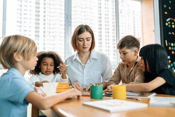 Teacher is teaching student about lesson from the books in the classroom, the children are happy. Some ask teacher, a boy in blue shirt is reading a book on his own and a girl is drawing. Erudition.