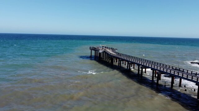 Vista de un muelle de pescadores con el mar en distintas tonalidades y oleaje fuerte