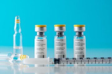 Vaccine vial glass with a syringe on blue background. Medicine vaccination concept. World pandemic concept.
