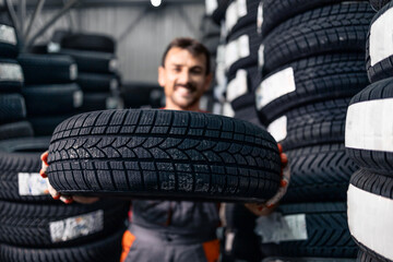 Tire shop worker standing in warehouse and holding brand new tires for sale.