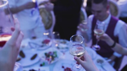 Group of guests celebrate and raise glasses, cheering with alcohol glasses with wine and champagne in the restaurant on corporate christmas birthday party event or wedding celebration, luxury event