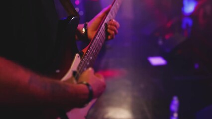 Concert view of an electric guitar player with vocalist and rock band performing in club, male musician guitarist on stage with audience in a crowded concert hall arena, live music show, slow motion
