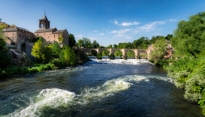 Obraz premium Scenic river flowing through lush greenery with a bridge and buildings