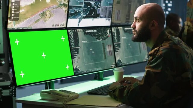 Army soldier looking at chroma key screens in command center housing operational missile defense system designed to intercept ballistic rockets. Specialist using mockup tracking gear, camera A