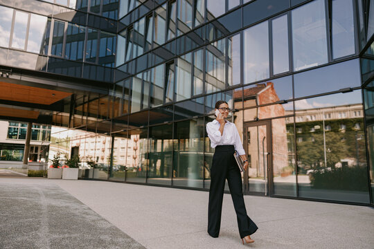 A confident businesswoman is walking in front of a modern glass building in the city