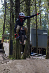 A rider performs a jump on an electric unicycle in a forested area near a bike park during daytime © Wanderson