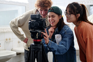 Group of three young people enthusiastically analyzing camera setup in a well-lit room while...