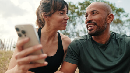 Close-up of athletic couple in love relaxing and using smartphone, front view