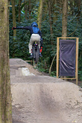 Mountain biker on an electric unicycle performs a jump on dirt ramps in a forest during daytime © Wanderson