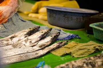 Fresh ribbonfish lined up on a stall with typical market utensils in the background.