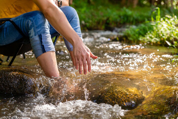 Happy Asian man enjoy outdoor lifestyle travel nature hiking and camping at forest mountain on summer holiday vacation. Healthy guy relaxing on outdoor chair in the stream and looking beautiful nature