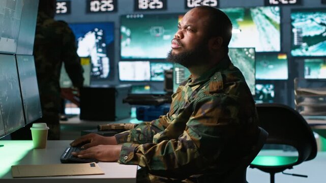 Officer in command center helped by colleague to plan, analyze and gather information on enemy troops. Team of agents in base of operations doing assessment of adversaries vulnerabilities, camera A