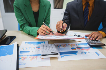 Asian business team engages in a collaborative meeting, financial charts at a desk. Dressed in formal suits, they brainstorm creative ideas to enhance company performance and team cohesion.