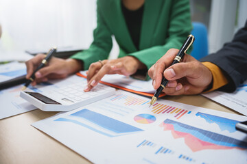 Asian business team engages in a collaborative meeting, financial charts at a desk. Dressed in formal suits, they brainstorm creative ideas to enhance company performance and team cohesion.