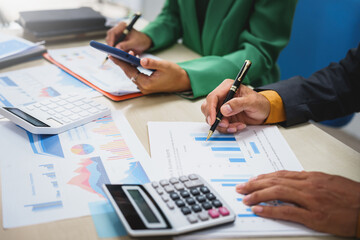 Asian business team engages in a collaborative meeting, financial charts at a desk. Dressed in formal suits, they brainstorm creative ideas to enhance company performance and team cohesion.