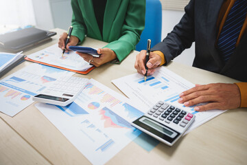 Asian business team engages in a collaborative meeting, financial charts at a desk. Dressed in formal suits, they brainstorm creative ideas to enhance company performance and team cohesion.