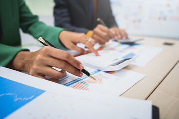 Asian business team engages in a collaborative meeting, financial charts at a desk. Dressed in formal suits, they brainstorm creative ideas to enhance company performance and team cohesion.