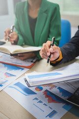 Asian business team engages in a collaborative meeting, financial charts at a desk. Dressed in formal suits, they brainstorm creative ideas to enhance company performance and team cohesion.