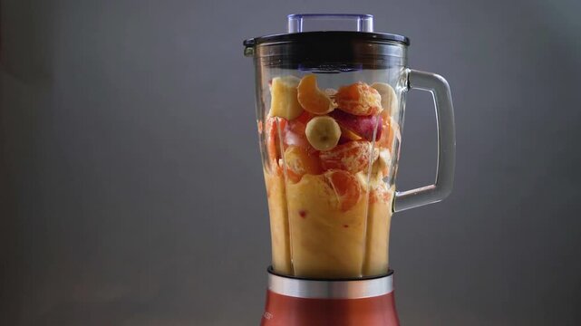 Mixing fresh fruit smoothie in a blender with bananas, oranges, and apples