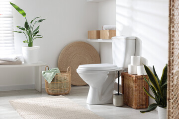 White toilet bowl, paper rolls and houseplants in bathroom