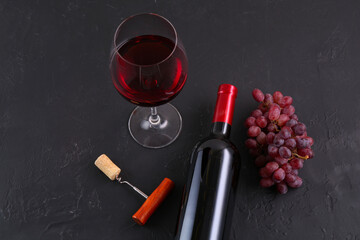 Corkscrew, glass of wine, bottle and grapes on black table, above view