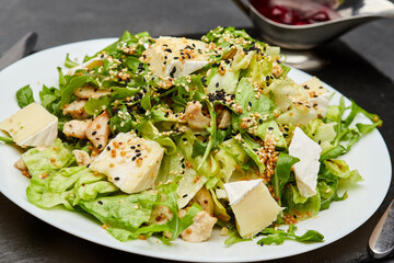 Fresh green salad with chicken, brie cheese, and sesame seeds, served with berry sauce on the side