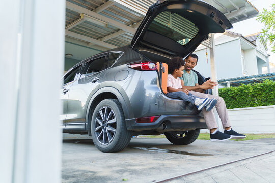 Black African American Father and son sitting in the open trunk of an SUV in a garage. Outdoor lifestyle and family bonding concept.