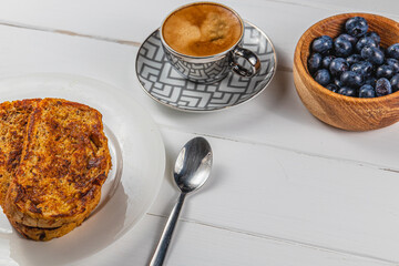 French toast on a white plate with blueberries and coffee for breakfast