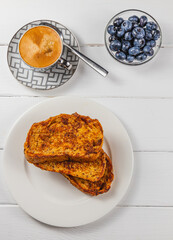 French toast on a white plate with blueberries and coffee for breakfast