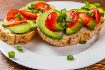 Avocado toast topped with tomato and green onion on a slice of carrot bread