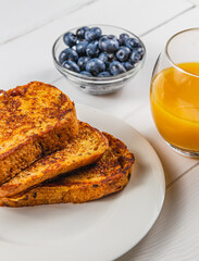 French toast on a white plate with blueberries and orange juice for breakfast