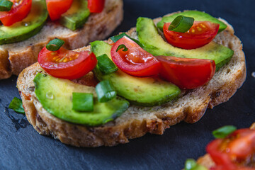 Avocado toast topped with tomato and green onion on a slice of carrot bread