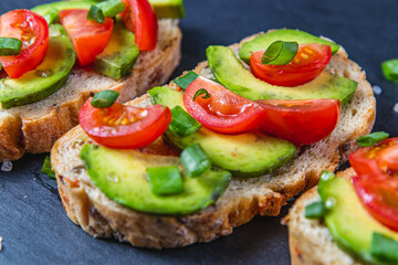 Avocado toast topped with tomato and green onion on a slice of carrot bread