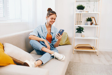 Happy Woman Holding Mobile Phone and Enjoying Relaxation on Cozy Sofa in Living Room
