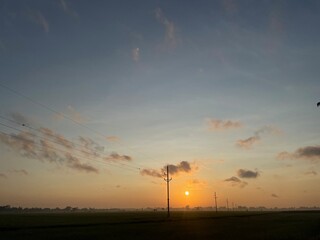 Fototapeta premium Silhouette electric pole and high voltage tower.High voltage transmission pole against morning sun in rice fields background.