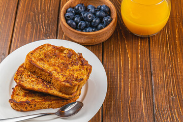 French toast on a white plate with blueberries and orange juice for breakfast