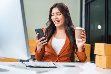 A young Asian businesswoman sits at her table, watching the computer screen.She analyzes, plans, and sells products online from home, smiling as she replies to comments and takes orders successfully.