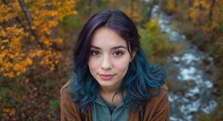 Fototapeta premium Young woman with vibrant blue and purple hair smiles joyfully outdoors, autumn foliage visible in background