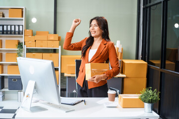 A beautiful businesswoman works at her desk, selling products online. She smiles as she looks at...