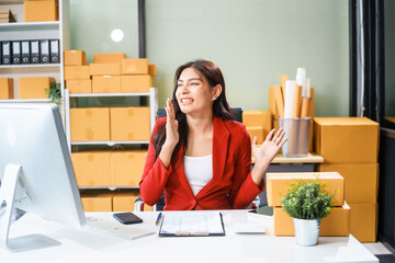 A beautiful businesswoman sits at the table, looking at the computer screen and talking on the phone. She analyzes marketing plans with a smile, feeling happy and successful in her online business.