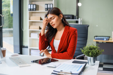 An Asian businesswoman sits at the table, working long hours as a financial analyst on computers  tablets.experiences office syndrome symptoms like neck pain, headaches, stress,other health issues.