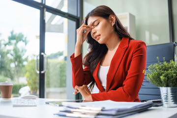 Obraz premium An Asian businesswoman sits at the table, working long hours as a financial analyst on computers tablets.experiences office syndrome symptoms like neck pain, headaches, stress,other health issues.