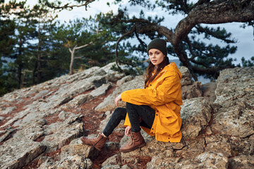 A woman in a yellow coat enjoying the serene beauty of nature on a rocky hill surrounded by trees