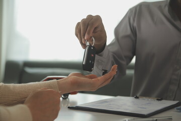 Young man receives a key from car salesman. After agreeing to a contract for rent or sale of a car at workshop, loan car, insurance, sale, buying car and finance concept.