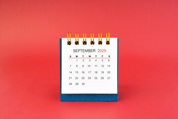 September 2025 white desk calendar on red background.