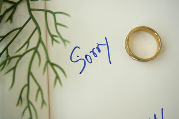 Note with the sorry word next to a wedding ring.