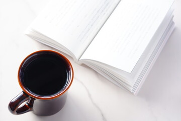 テーブルの上の開いた本とコーヒーカップで、コーヒーを飲みながら読書を楽しむイメージ
