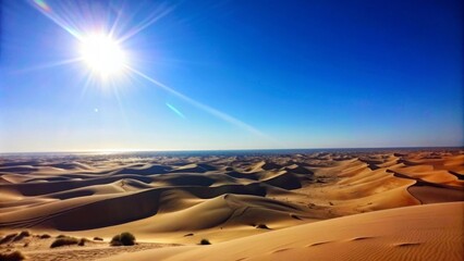 Naklejka premium A vast, golden desert stretches out under a clear blue sky, with a bright sun casting long shadows on the sand dunes. The image evokes feelings of heat, vastness, and the beauty of nature.