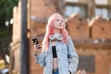 Fototapeta premium A girl with pink hair is holding a cell phone and wearing headphones