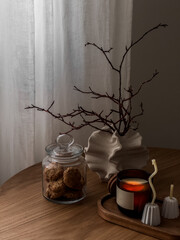 A cozy autumn composition on a round wooden table - a cookie jar, an autumn bouquet, lighted candles. Cozy house concept